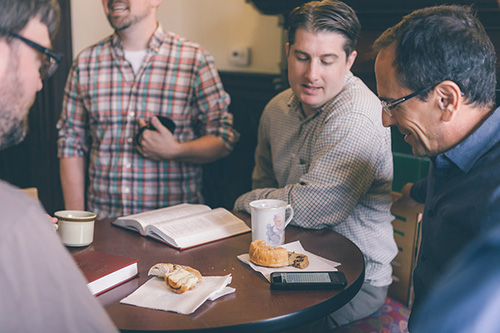 Group of men studying the bible while eating coffee cakes and drinking coffee